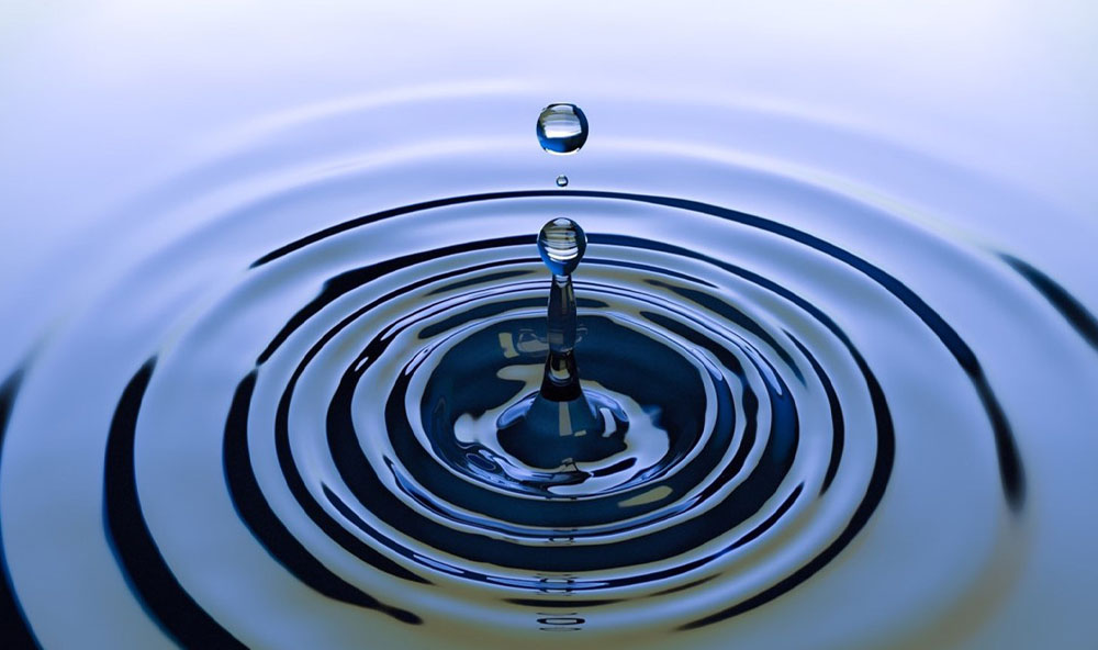 A photograph of a drop of water splashing and making ripples on the surface of the water.