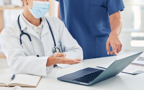 Two medical professionals looking at a laptop in a doctors office.