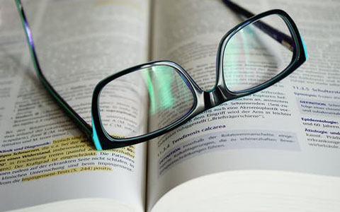 Reading glasses placed on an open book. Some of the text in the book is highlighted.